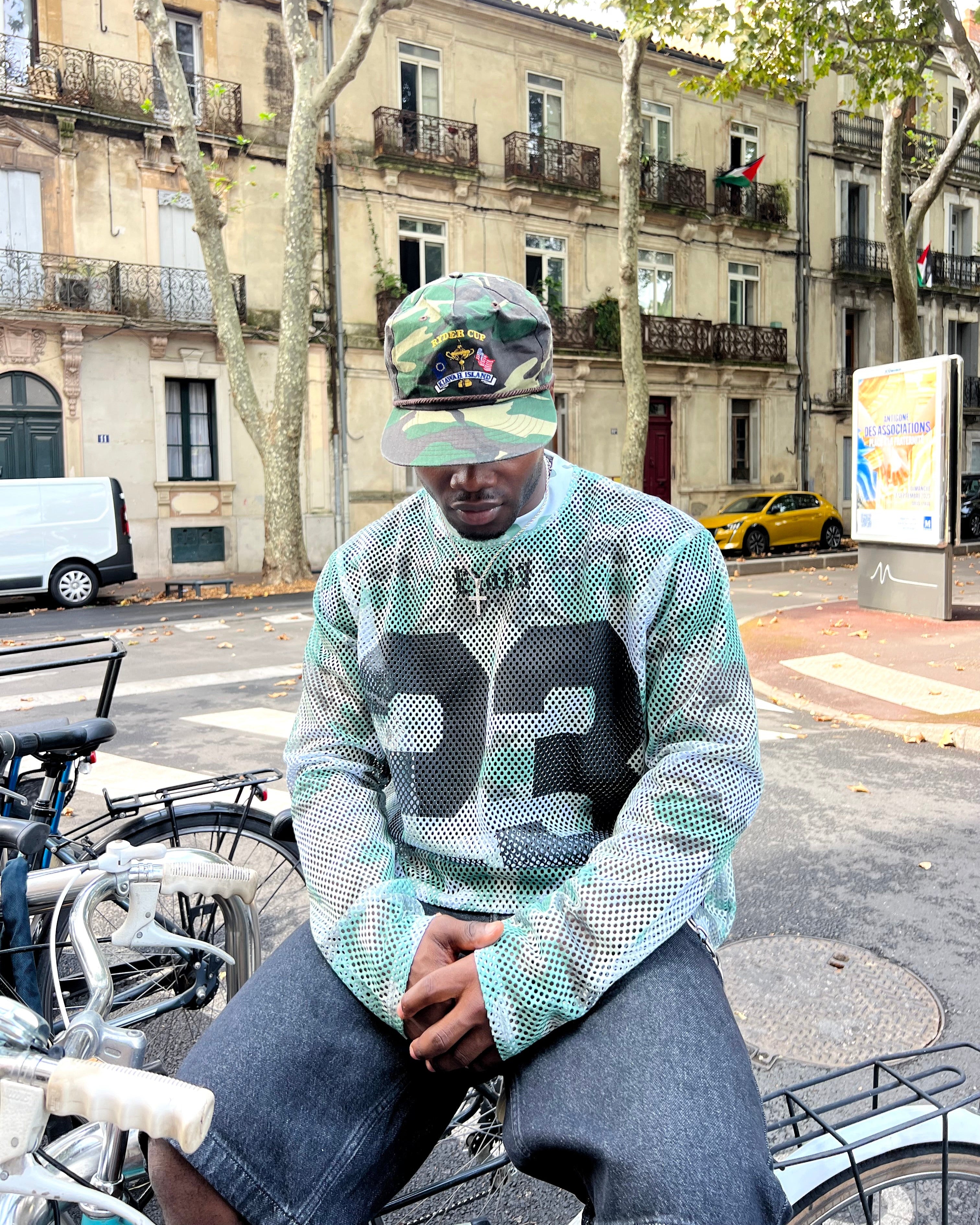 Person wearing a patterned sweater and cap sitting on a bicycle in an urban setting.