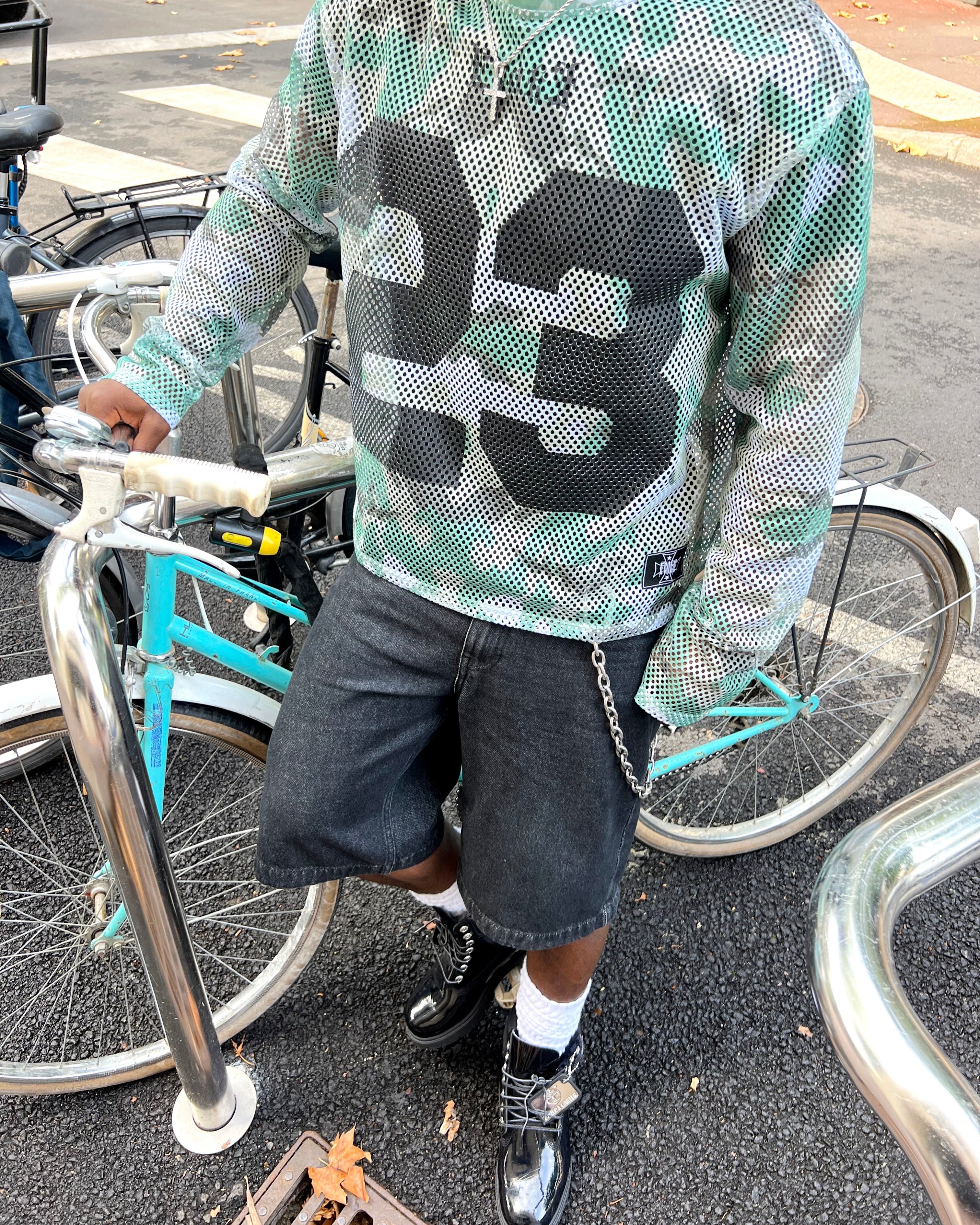 Person wearing a green and black patterned shirt with a bicycle in the background