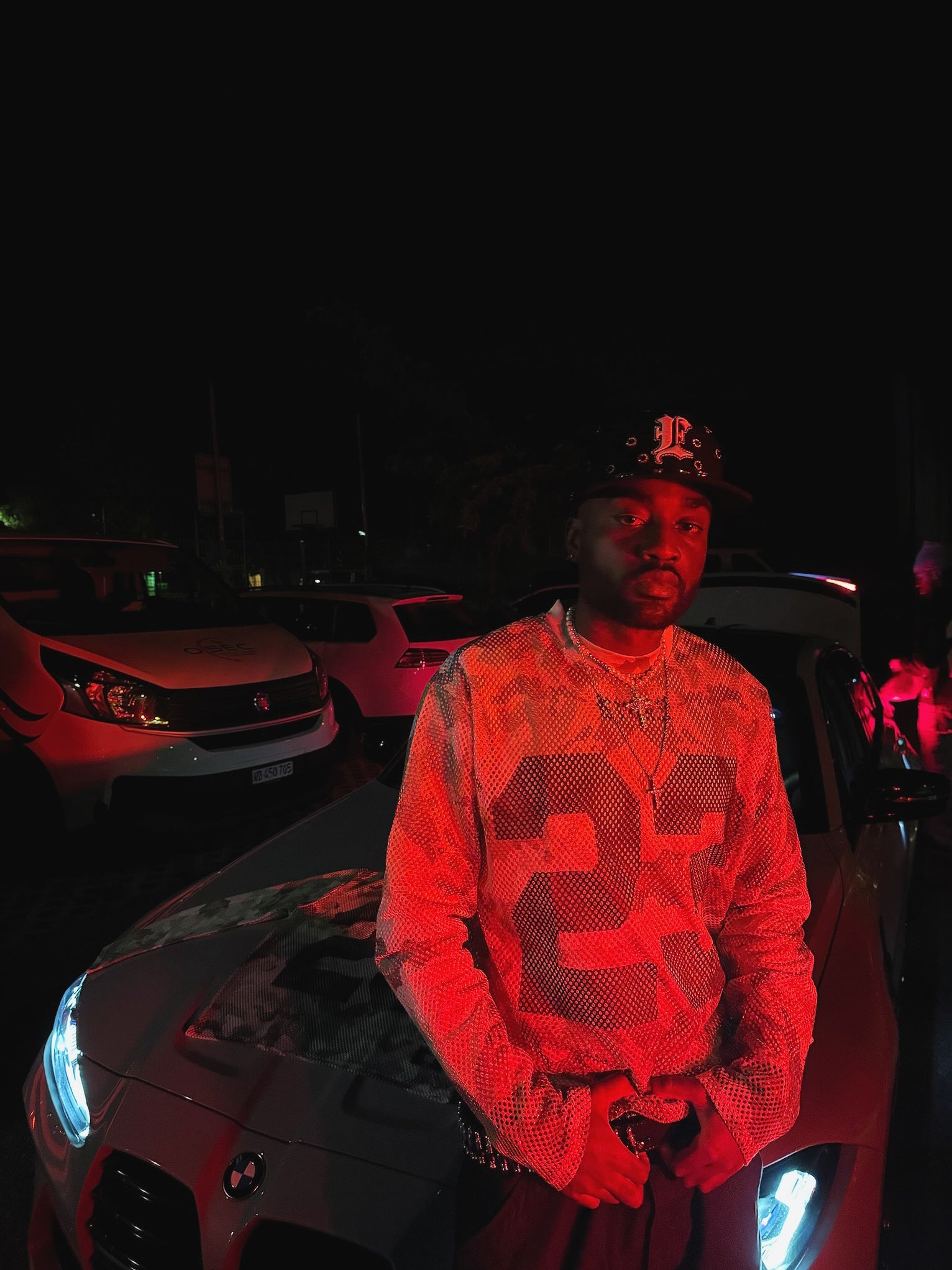 Person wearing a reflective jacket with numbers, standing next to a car at night.
