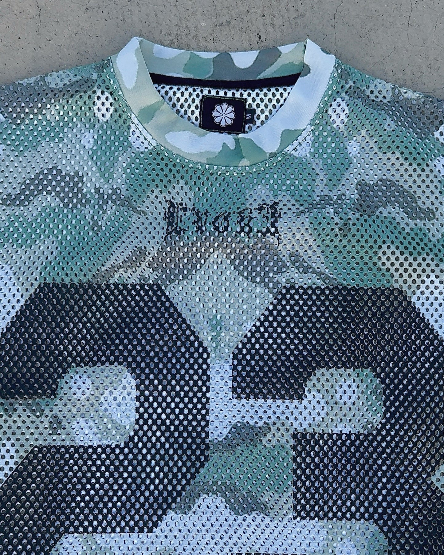 Camouflage-patterned shirt with brand logo on a concrete surface