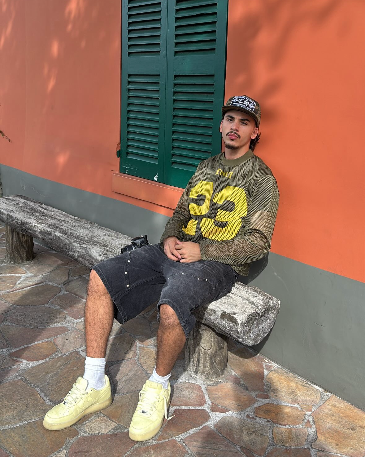 Person sitting on a stone bench against an orange wall with green shutters.
